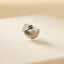 A silver earring in the shape of a seashell is resting on a light-colored surface.