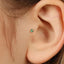 A close-up view of a person's ear, focusing on a small green gemstone or piercing in the earlobe.