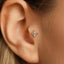 A close-up view of a person's ear, showing a small gold earring with a diamond-like center stone.
