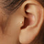 A close-up view of a person's ear, showing a small gold earring in the earlobe.