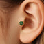 A close-up of a person's ear with a green gemstone earring featuring a star-shaped design.