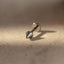 A close-up image of a metal piercing, specifically a metal stud or earring, resting on a textured surface.