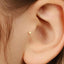 A close-up view of a person's ear, showing a small gold-colored earring or stud inserted into the earlobe.
