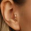 A close-up view of a person's ear, showing a gold earring with a small gemstone dangling from it.