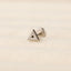 A silver-colored metal earring in the shape of a triangle is shown against a light-colored background.