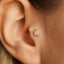 A close-up of a person's ear with a small, gold-colored earring featuring a crescent moon design.