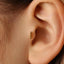 A close-up view of a person's ear, showing a small gold-colored earring with three small balls protruding from it.