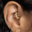 A close-up view of a person's ear with a gold-colored metal earring in the earlobe.
