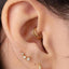 a close-up view of a person's ear adorned with multiple gold earrings, including a hoop earring and three small diamond earrings.
