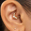 A close-up of a person's ear with a gold hoop earring and a diamond-encrusted ring.