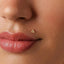A close-up of a person's face, focusing on their lips and a small gold-colored triangle-shaped piercing in their nose.