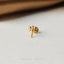 A small gold earring in the shape of a dragonfly is resting on a white surface.
