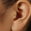 A close-up of a person's ear with a small gold earring in the earlobe.