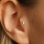 A close-up view of a person's ear, showing a small silver crescent moon-shaped earring in the earlobe.