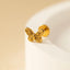 A gold-colored butterfly-shaped earring is resting on a white surface.