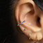 A close-up view of a person's ear adorned with multiple jewelry pieces, including a ring with blue gemstones and hoop earrings.