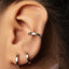 A close-up view of a person's ear adorned with three silver earrings, including a ring and two hoop earrings.
