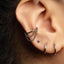 A close-up view of a person's ear adorned with multiple silver earrings, including a hoop earring and a chain earring.