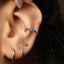 A close-up view of a person's ear adorned with multiple earrings, including a ring with blue stones and a hoop earring.