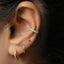 A close-up view of a person's ear adorned with multiple earrings, including a turquoise-colored cork earring and a gold hoop earring.