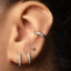 A close-up view of a person's ear adorned with multiple silver earrings, including a cork clip and three hoop earrings with rhinestones.