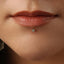 A close-up of a person's face, focusing on their lips and a small, round, blue gemstone piercing in the lip.