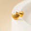 A gold-colored shell-shaped earring is resting on a white surface.