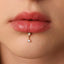 A close-up of a person's lips with a gold-colored earring featuring a small opal stone hanging from it.