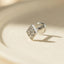 A small diamond-shaped earring with a clear gemstone set in the center, resting on a light-colored surface.