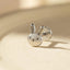 A silver earring in the shape of a bunny's head is sitting on a light-colored surface.