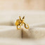 A gold-colored earring in the shape of a pair of scissors is shown against a blurred background.