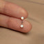 A close-up image of a person's thumb holding a small earring with two opal stones.
