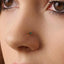 A close-up of a person's nose with a small gold-colored nose stud featuring a green gemstone.