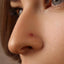 A close-up of a person's nose with a small red gemstone or piercing in it.