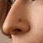 A close-up of a person's face, focusing on their nose and the red gemstone piercing.