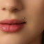 A close-up of a person's face, focusing on their lips and a small gold-colored stud or piercing in their lip.