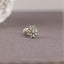 A silver-toned flower-shaped earring with a small center stone is displayed on a gray fabric surface.