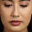 A close-up of a woman's face, focusing on her nose and lips. She is wearing a gold nose ring with a diamond accent.
