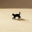 A small black cat figurine is standing on a light brown surface, casting a shadow.