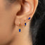 A close-up view of a person's ear adorned with a pair of gold earrings featuring blue gemstones.