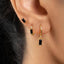 A close-up view of a person's ear adorned with three gold earrings, each featuring a black gemstone.