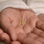 A close-up image of a person's hand holding a small gold-colored flower-shaped charm.