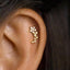A close-up of an ear with a delicate gold earring featuring a small flower design.