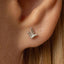 A close-up of a person's ear with a small, silver earring featuring a leaf-like design.