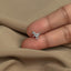 A person's thumb is holding a small silver earring in the shape of a dinosaur.
