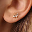 A close-up view of a person's ear adorned with a delicate gold earring featuring a small flower-like design.