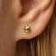 A close-up of a person's ear with a small gold-colored earring featuring a geometric design.