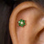 A close-up of a person's ear with a small, green gemstone flower-shaped earring with a diamond in the center.