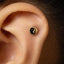 a close-up view of a person's ear, with a small gold-colored earring featuring a black and white symbol, such as a yin and yang symbol, embedded in the skin.
