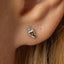 A close-up view of a person's ear with a small silver earring featuring a hand design.